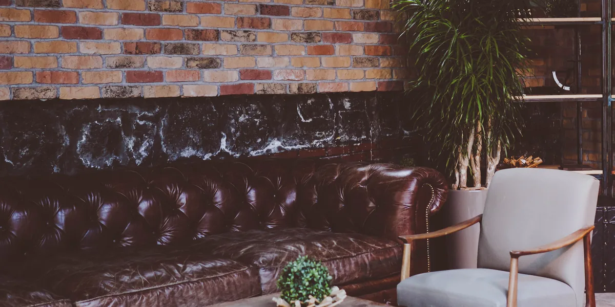 Ledersofa mit Knopfheftung und grauer Sessel vor einer Ziegelwand