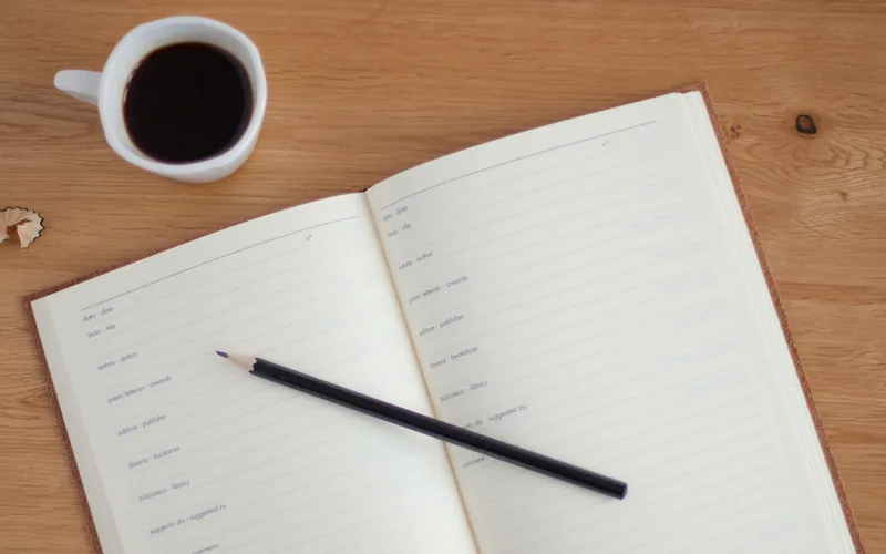 Aufgeschlagenes Lesejournal mit Bleistift neben einer Tasse Kaffee